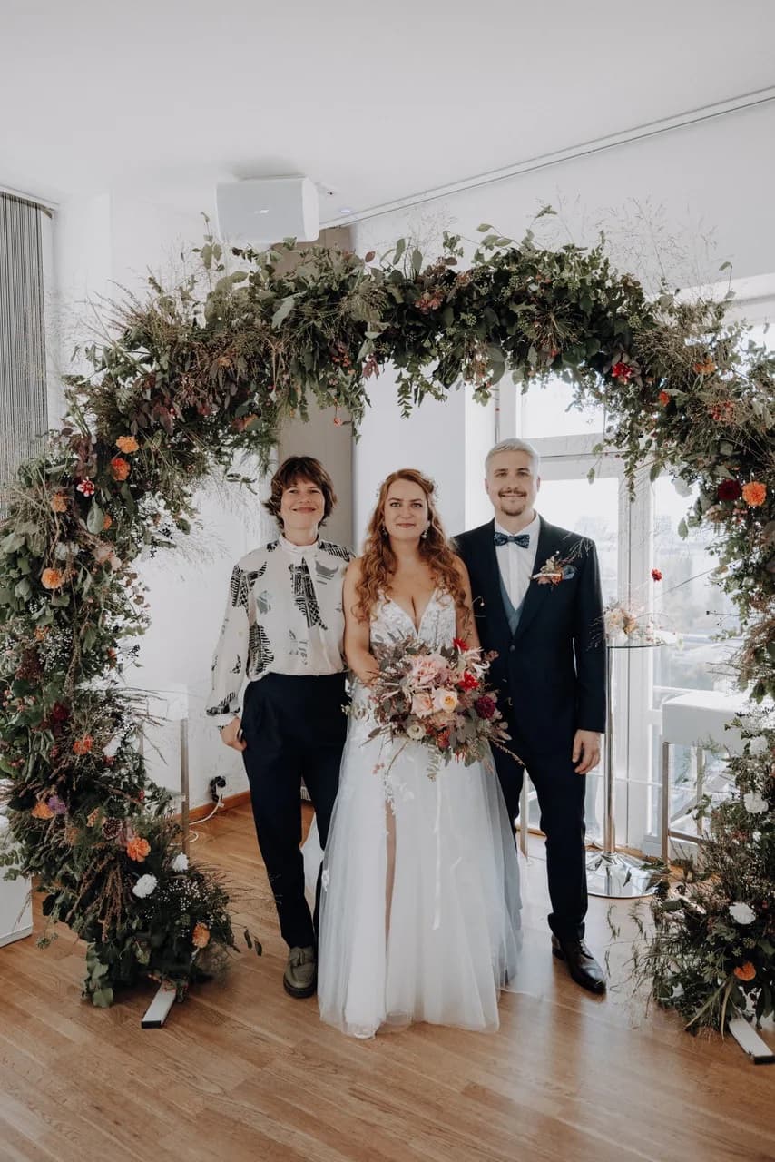 Freie Trauung unter Blumenbogen — Traurednerin Katharina Göbel mit Brautpaar